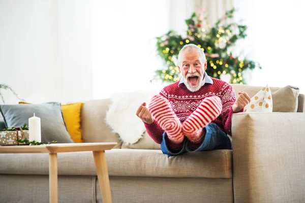 Ένα χαρούμενο ανώτερος άνθρωπος με κόκκινες και λευκές κάλτσες στο σπίτι στο χρόνο Χριστουγέννων, διασκέδαση. — Φωτογραφία Αρχείου