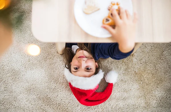 Una vista superior de una niña pequeña con sombrero de Santa alcanzando para galletas en época de Navidad . —  Fotos de Stock