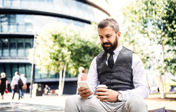 Hipster işadamı kahve ve açık havada şehirde oturan smartphone ile. — Stok fotoğraf
