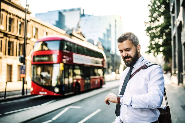 Hipster affärsman stående på gatan i London, kontroll av tid. — Stockfoto