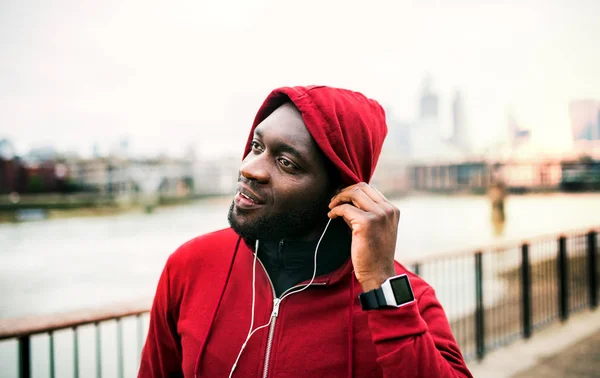 Fekete férfi futó kapucnival a fején, a város és a fülhallgató közelről. Másolja a hely. — Stock Fotó