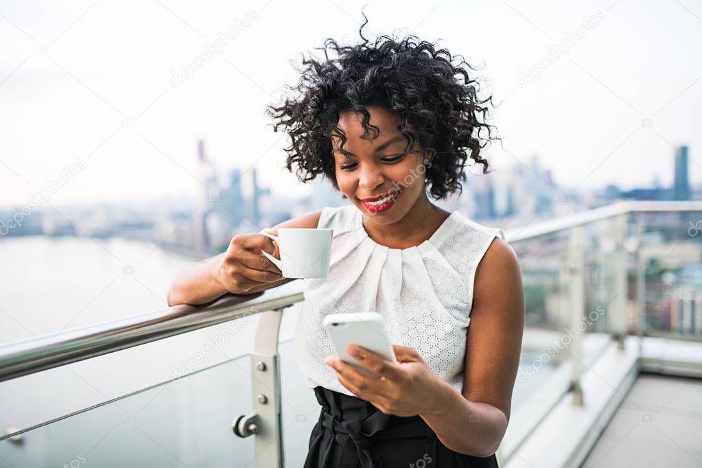 A businesswoman with coffee and smartphone standing against London view panorama.