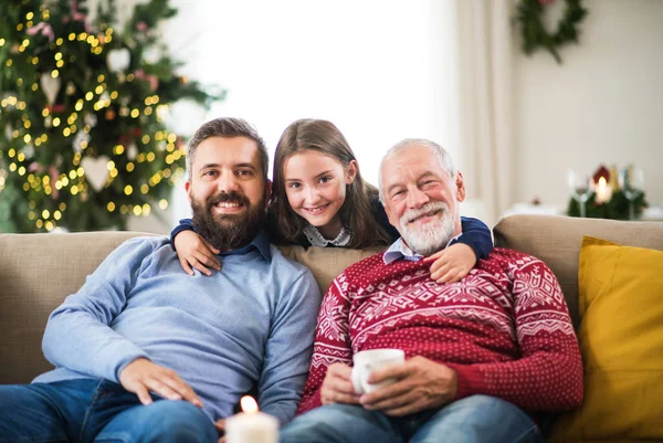 Menina pequena e seu pai e avô sentados em um sofá no Natal . — Fotografia de Stock