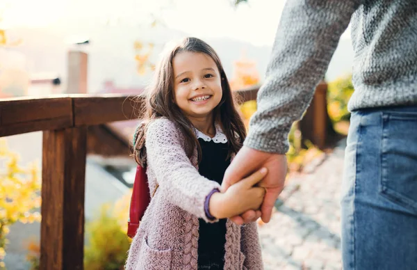 Una niña pequeña sosteniendo una mano de un padre irreconocible en un paseo en otoño . — Foto de Stock