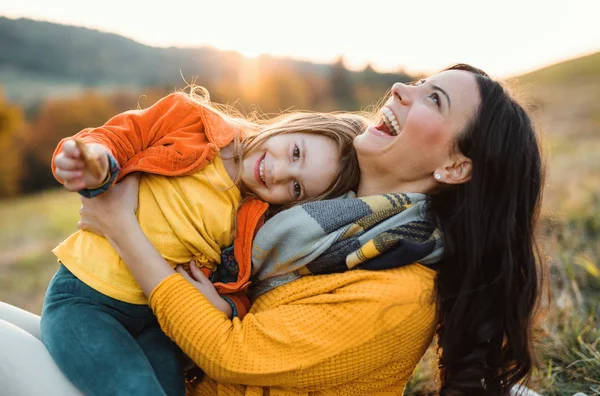 Um retrato da jovem mãe com uma pequena filha no outono natureza ao pôr do sol. — Fotografia de Stock