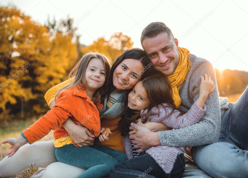 A portrait of young family with two small children in autumn nature at sunset.