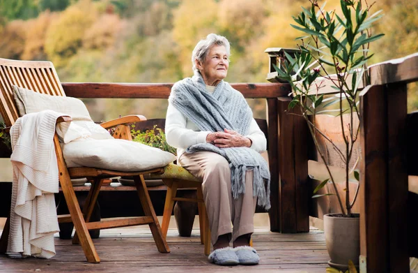 Una donna anziana seduta all'aperto su una terrazza in una giornata di sole in autunno . — Foto Stock