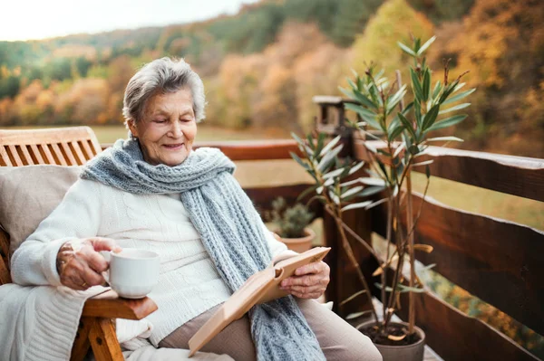 An elderly woman reading book outdoors on a terrace on a sunny day in autumn. — Stock Photo, Image