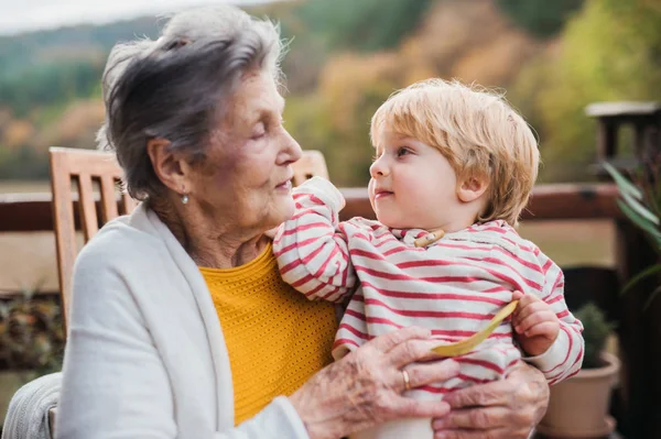 Äldre kvinna med en småbarn barnbarnsbarn på en terrass i höst. — Stockfoto