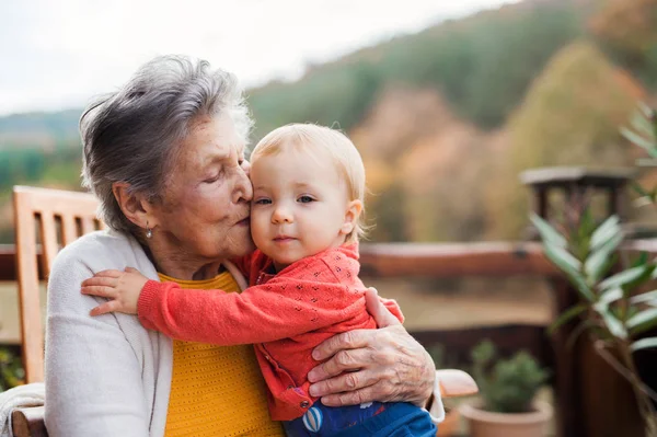 Elderly woman kissing a toddler great-grandchild on a terrace in autumn. — Stock Photo, Image