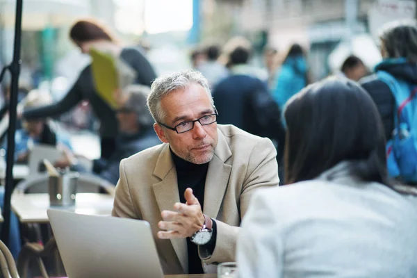 Man en vrouw business partners met laptop zitten in een cafe in stad, praten. — Stockfoto