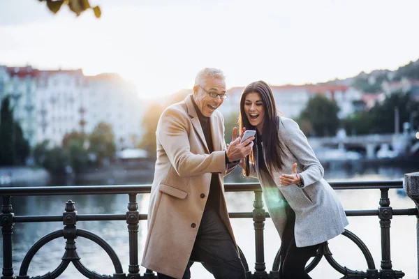 Muž a žena a obchodním partnerům smartphone stojící ve městě, vyjadřuje vzrušení. — Stock fotografie