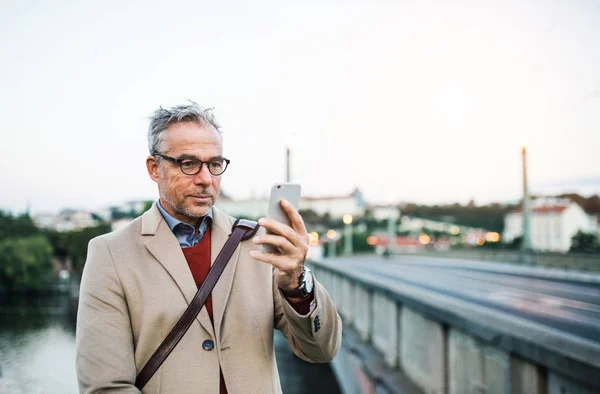 Starší podnikatel s smartphone stojí u řeky ve městě Praha, přičemž selfie. — Stock fotografie