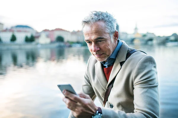 Dojrzałe biznesmen z smartphone stojący nad rzeką Wełtawą w Prague city. — Zdjęcie stockowe