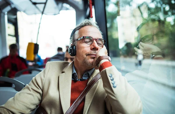 Dojrzałe zmęczony biznesmen z heaphones podróż autobusem w mieście. — Zdjęcie stockowe