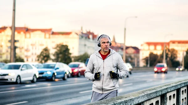 ヘッドフォンの屋外を実行するプラハ市内の橋の上で成熟した男性ランナー. — ストック写真