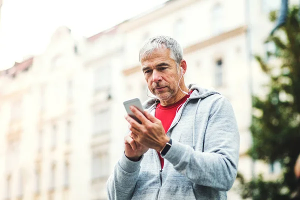 Ένα πορτρέτο του ένα ενεργό ώριμος άνδρας στέκεται σε εξωτερικούς χώρους στην πόλη, χρησιμοποιώντας το smartphone. — Φωτογραφία Αρχείου
