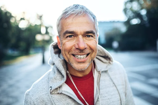 Portrait d'un homme mature actif debout à l'extérieur en ville, vêtu d'une capuche . — Photo