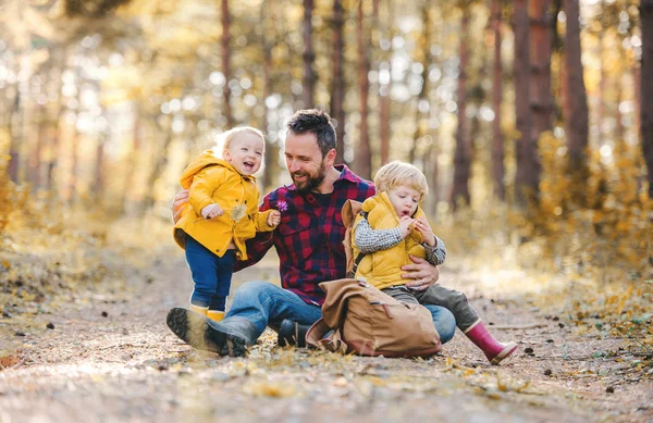 Взрослый отец с маленькими детьми, сидящими на земле в осеннем лесу . — стоковое фото