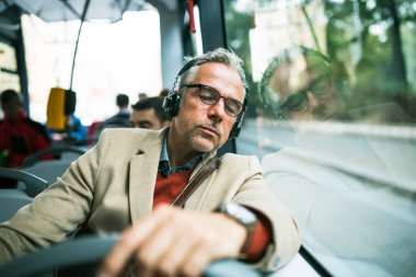 Müzik olgun yorgun işadamı otobüsle şehir, gözlük ve heaphones travellling ile.