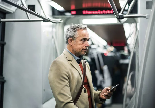 Зрелый бизнесмен со смартфоном путешествует на метро по городу . — стоковое фото