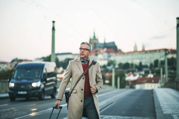 Uomo d'affari maturo con valigia a piedi su un ponte nella città di Praga . — Foto Stock