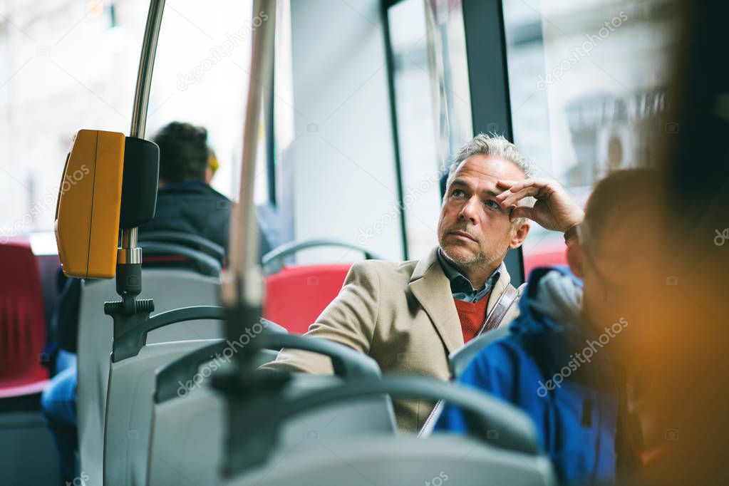 Tired mature businessman travelling by bus in city.