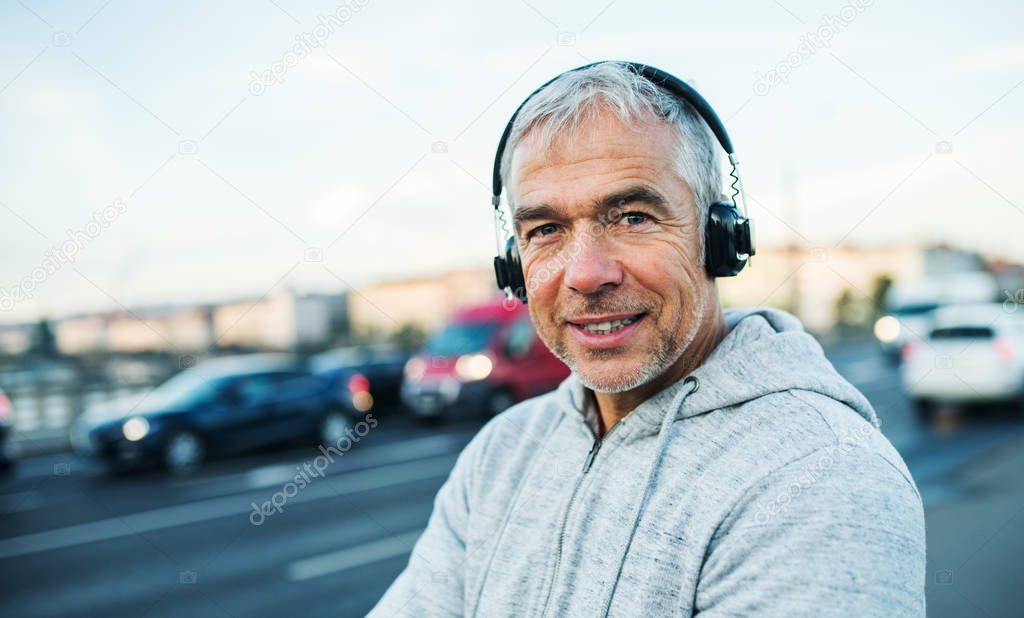 Mature male runner with headphones outdoors in city, listening to music.