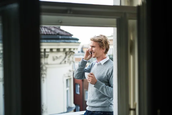 Jeune homme avec smartphone debout sur un balcon en ville, passer un appel téléphonique . — Photo