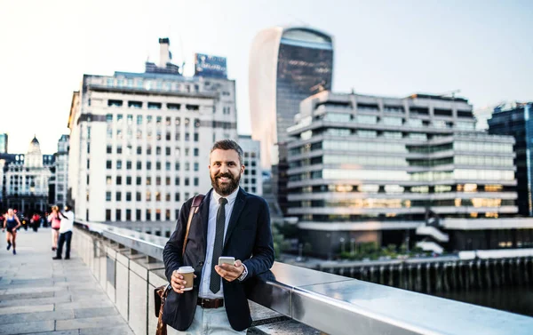 Hipster επιχειρηματίας με καφέ και smartphone στέκεται έξω στην πόλη. — Φωτογραφία Αρχείου