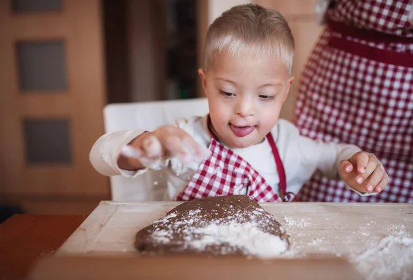 Een gehandicapte down syndroom kind met zijn moeder binnenshuis bakken. — Stockfoto