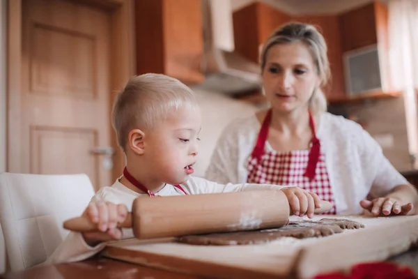 Handikappade Downs syndrom barn med sin mor inomhus bakning. — Stockfoto