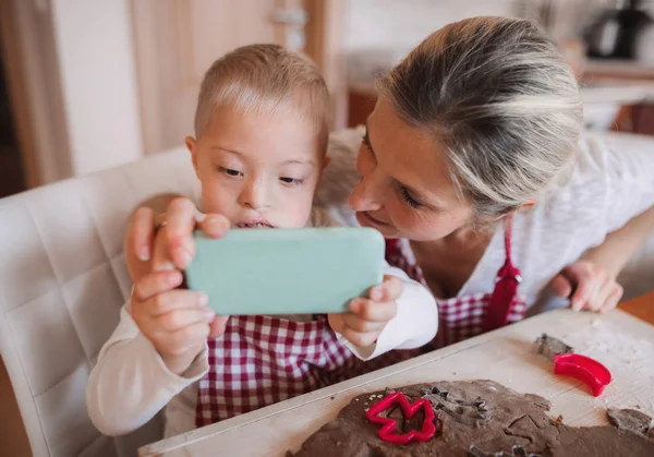 Downův syndrom dítě s matkou doma užívat selfie při pečení. — Stock fotografie