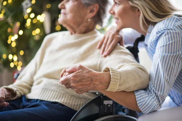 En äldre kvinna i rullstol med hälsa besökare hemma i juletid. — Stockfoto