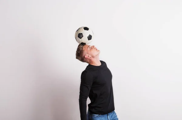 Portret van een jonge man met voetbal bal op kop in een studio. Kopiëren van ruimte. — Stockfoto