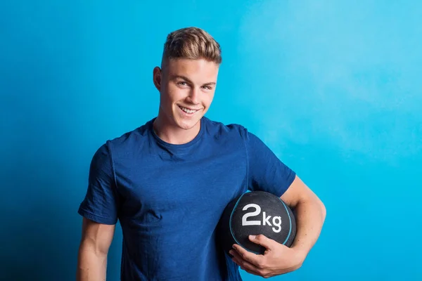 Portrait of a young man holding a heavy ball in a studio. — Stock Photo, Image