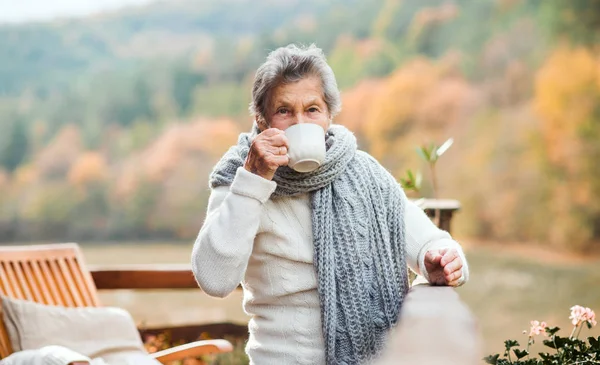 Eine ältere Frau trinkt im Herbst draußen auf einer Terrasse Kaffee. — Stockfoto