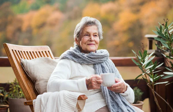Eine ältere Frau sitzt an einem sonnigen Herbsttag im Freien auf einer Terrasse. — Stockfoto