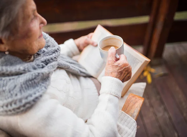 An elderly woman reading book outdoors on a terrace on a sunny day in autumn. — Stock Photo, Image