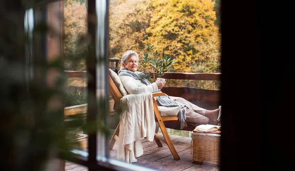 Una anciana sentada al aire libre en una terraza en un día soleado en otoño . — Foto de Stock