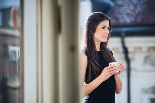 Молода бізнес-леді з чашкою кави, що стоїть на терасі в офісі в місті . — стокове фото