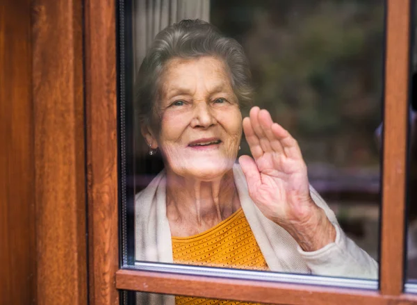 An elderly woman standing by the window, looking out. Shot through glass. Royalty Free Stock Photos