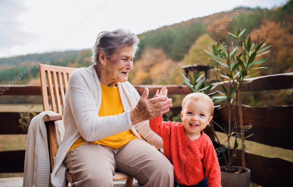 Elderly woman with a toddler great-grandchild on a terrace in autumn, giving high five.