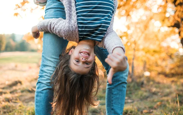 Um pai segurando uma pequena filha de cabeça para baixo na natureza outono . — Fotografia de Stock