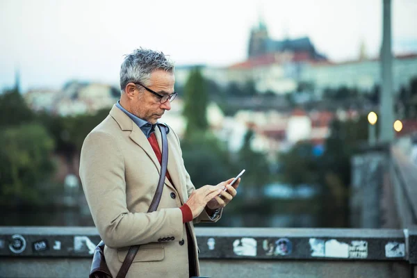 Biznesmen z smartphone stojąc na moście w mieście, wiadomości tekstowe. — Zdjęcie stockowe