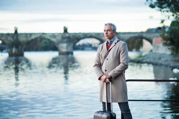 スーツケース プラハ シティのヴルタヴァ川のそばに立って、成熟したビジネスマン. — ストック写真