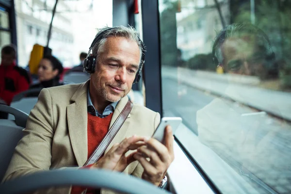 Зрілий втомлений бізнесмен з хефонами і смартфон, що подорожує на автобусі в місті . — стокове фото