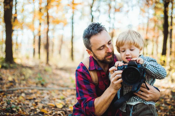 Starší otec a syn batole v podzimním lese, fotografování s fotoaparátem. — Stock fotografie