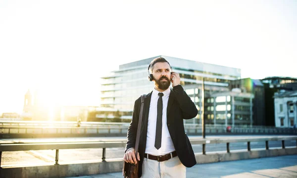 Hipster επιχειρηματίας με hadphones στέκεται έξω στην πόλη στο ηλιοβασίλεμα. — Φωτογραφία Αρχείου