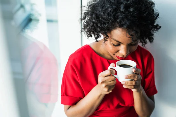 A close-up of a woman standing by the window holding a cup of coffee. — Stock Photo, Image